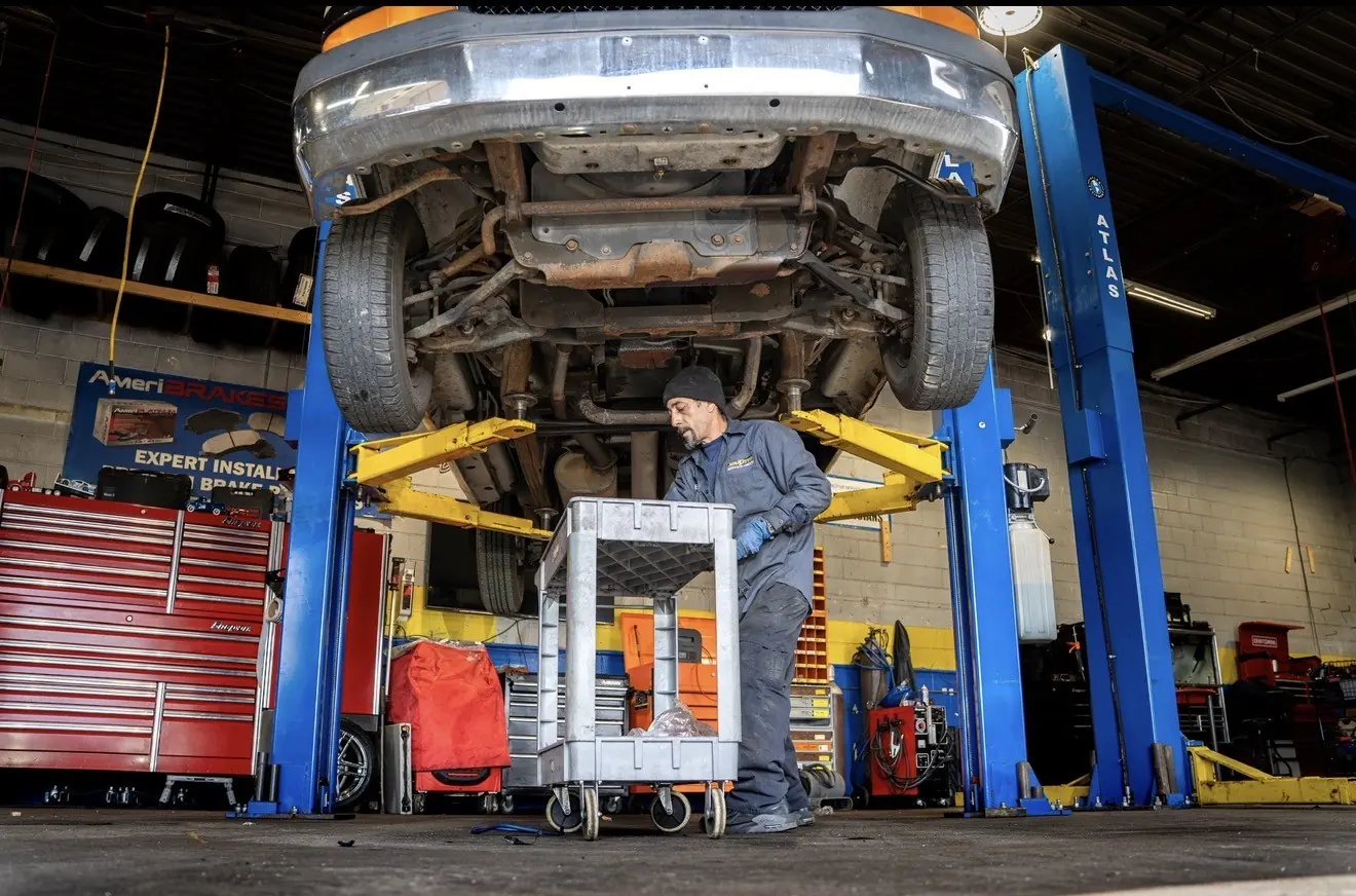 A technician under a raised vehicle with a transmission jack